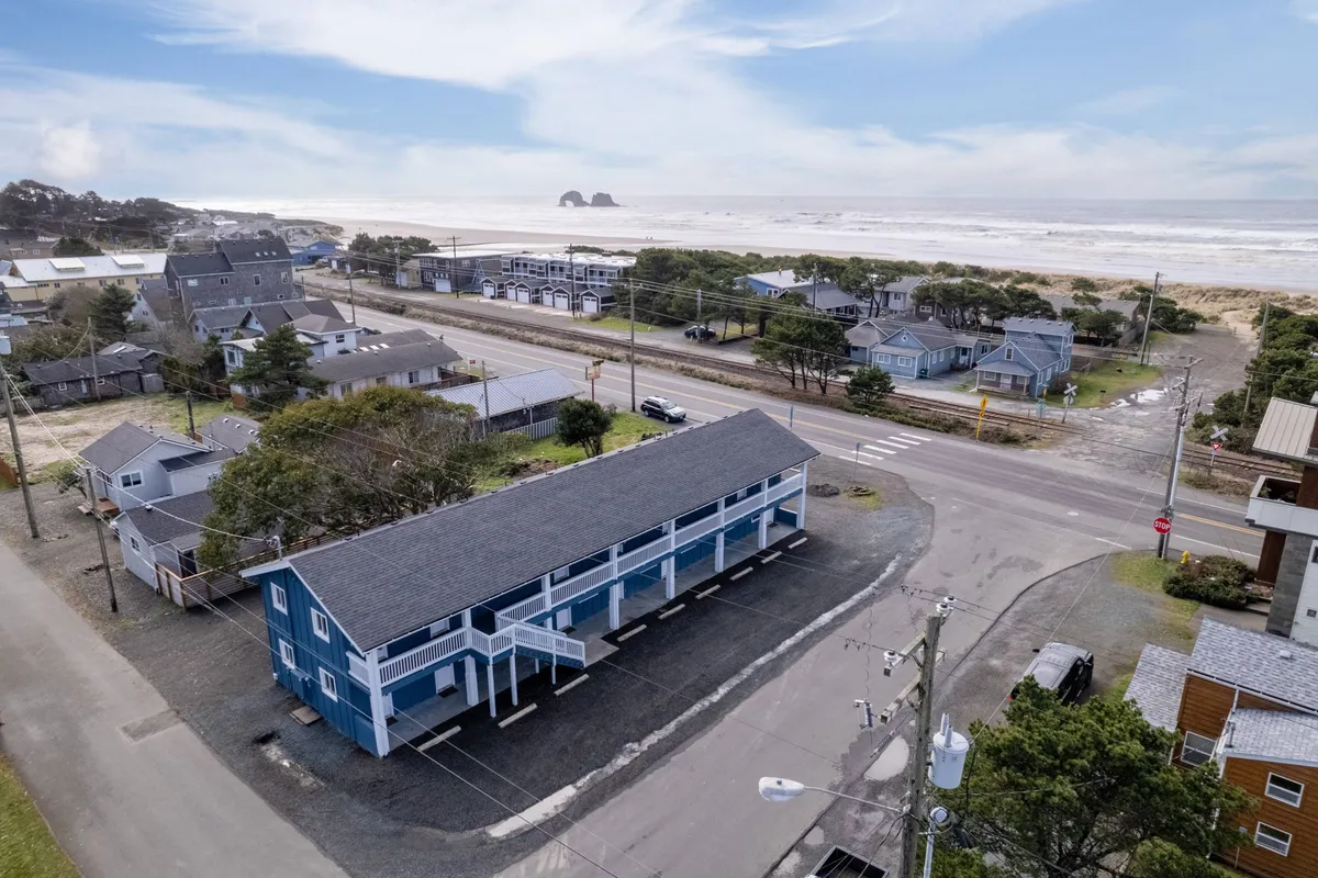 A relaxing exterior view featuring the blue building set against the ocean, with nearby sandy beach access and surrounding homes. The environment is perfect for morning or evening walks with pets and fosters a relaxed, cheerful mood.
