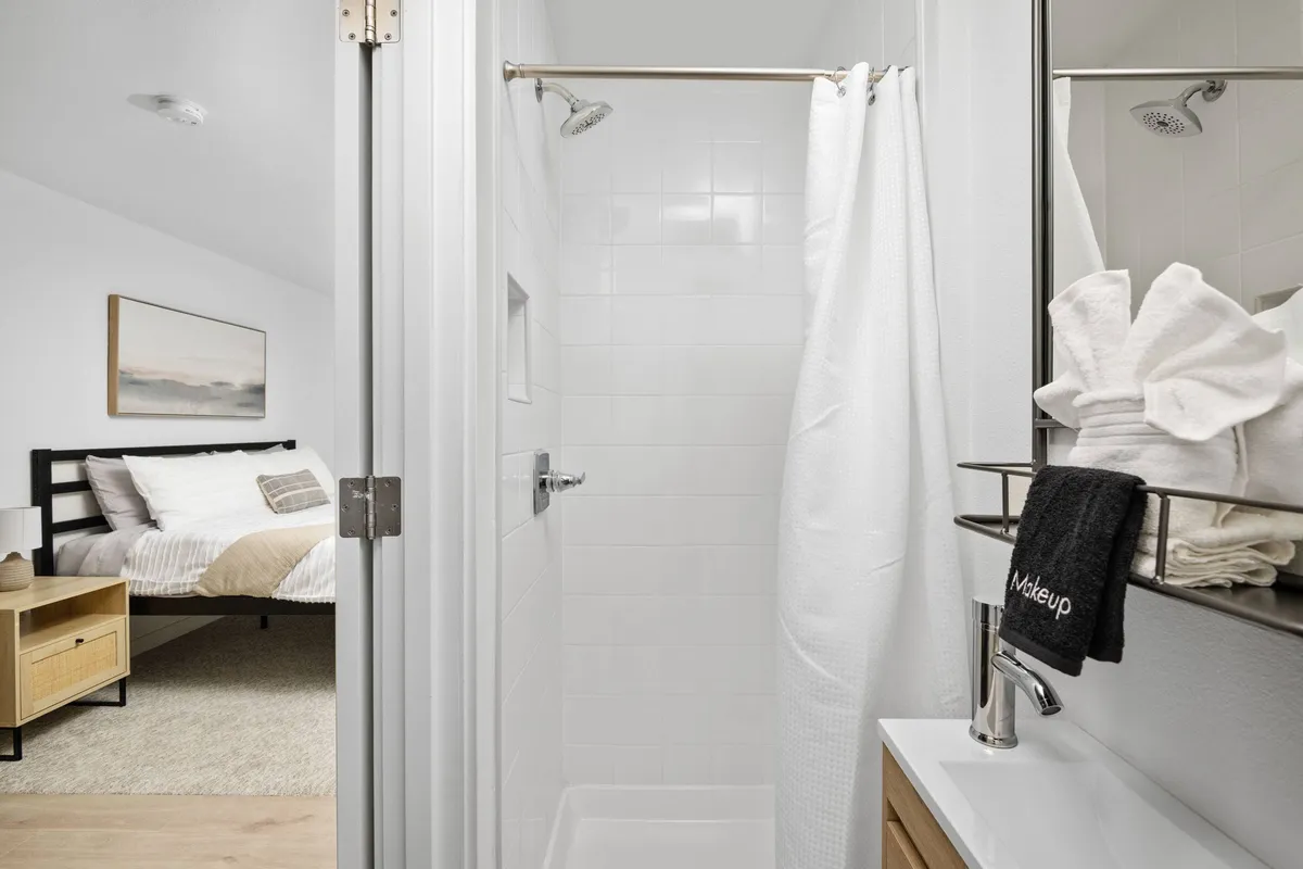 An inviting bathroom scene with a modern shower area, spotless sink, and plush towels, with a glimpse into a tidy bedroom in the background. The floors and surfaces are sleek and easy to clean—ideal for a pet-friendly setup.