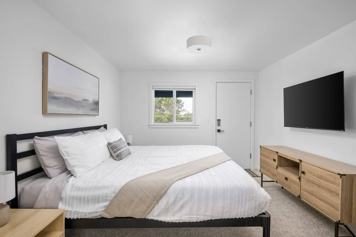 The scene centers around the neatly made bed, a wall-mounted TV, eye-catching artwork, and a window that hints at natural light. The overall atmosphere is peaceful and uncluttered, perfect for restful nights and leisurely mornings.