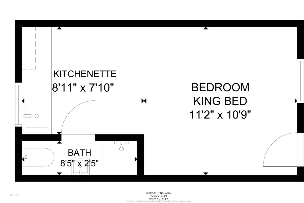 This inviting interior image features the king bed, a compact kitchenette, and a glimpse of the bathroom, all within one thoughtfully arranged space. The room looks freshly remodeled, with plush bedding and soft lighting that underscore a sense of warmth and relaxation.
