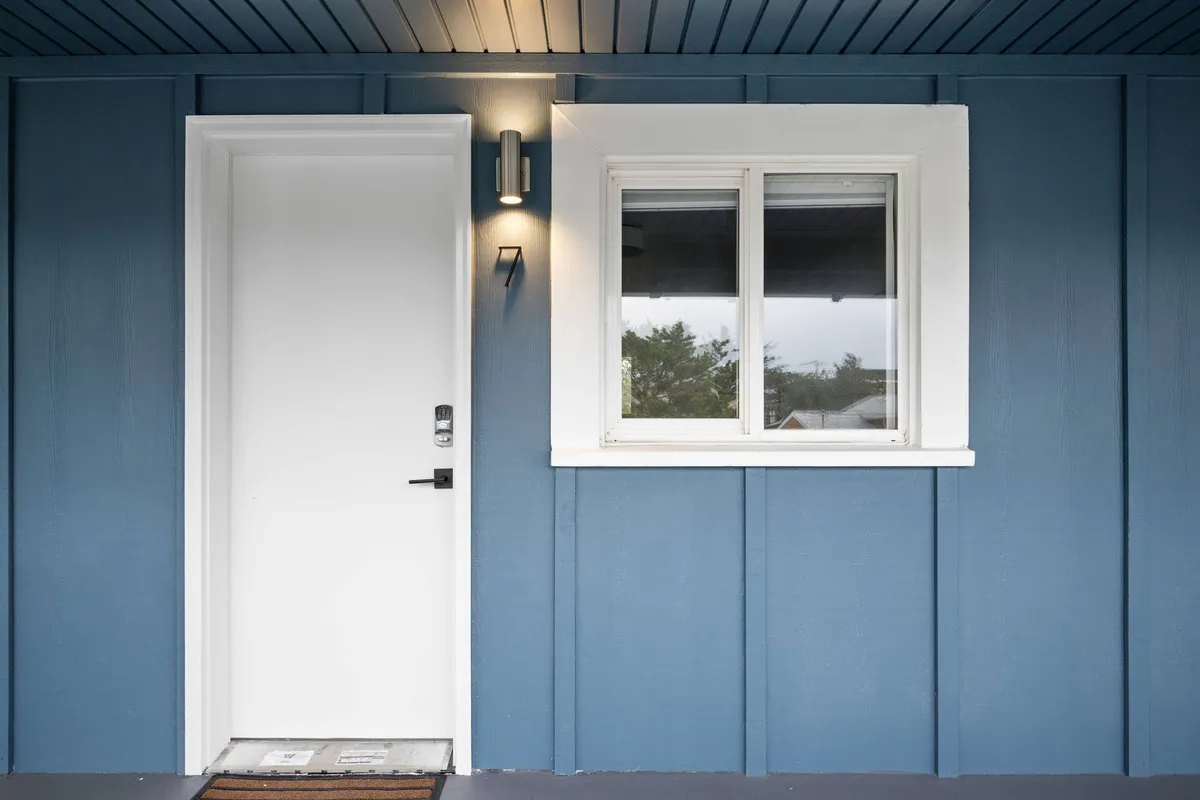 A close-up of the inn’s front door and window, featuring the building's distinct color and hints of seasonal decoration. The tidy entryway is styled to be inviting, emphasizing first impressions and the transition from the vibrant community outside to the serene privacy within.